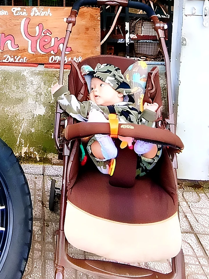 Em bé cười trong xe đẩy trước biển Tiệm Bánh An Yên ở Đà Lạt.